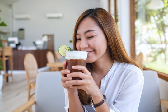 Portrait image of a beautiful young asian woman holding and drinking iced coffee in cafe