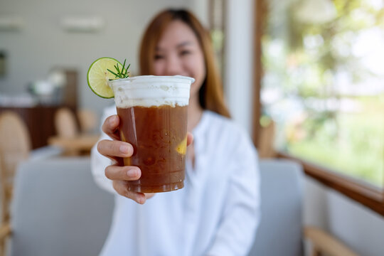 Portrait image of a beautiful young asian woman holding and serving a glass of iced coffee