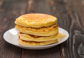 Stack of delicious pancakes in white plate on brown wooden background. It is a homemade breakfast Thick, soft, scented with butter.