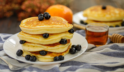 Sweet food. Stack of delicious pancakes with blueberries and honey, tea, plaid fabric in white plate on blur background.