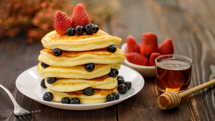 Sweet food. Stack of delicious pancakes with blueberries, Strawberry and honey in white plate on blur wooden background.