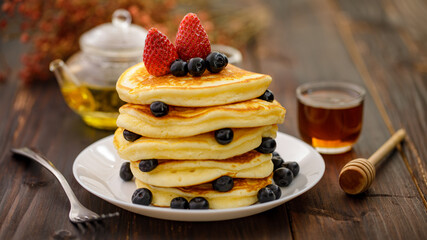 Sweet food. Stack of delicious pancakes with blueberries, Strawberry and honey in white plate on blur wooden background.