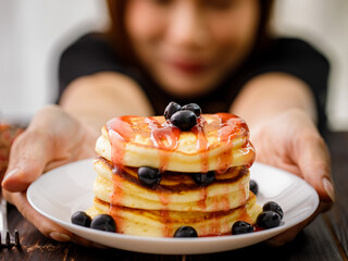 Close up hand Pancakes with strawberry jam, decorated with blueberry fruit in a white plate. Concept sweet food ready to serve.