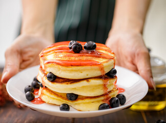 Close up hand Pancakes with strawberry jam, decorated with blueberry fruit in a white plate. Concept sweet food ready to serve.