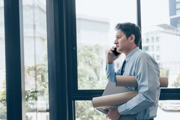 Busy businessman use mobile phone and hands hold dossier and drawing tube. Busy or a lot of work to...