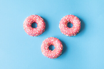 pink frosted donut with colorful sprinkles on blue background. copy space