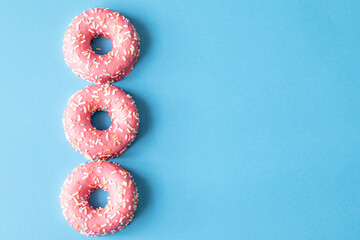 pink frosted donut with colorful sprinkles on blue background. copy space