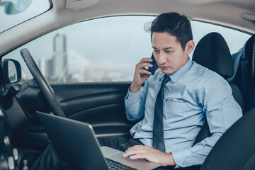 Businessman working in laptop and talking on the phone  in the drivers seat in his car.