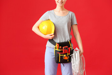 Young female electrician with tools on color background