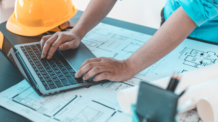 Young man with a laptop plotting a system of building structures in blueprints, Architects or...