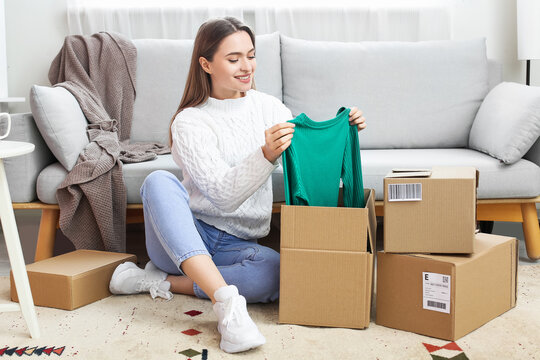 Young woman opening parcel with new clothes at home