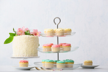 Dessert stands with tasty cupcakes and cake on light background