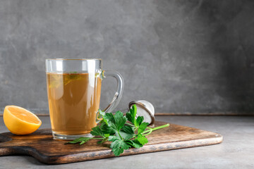 Board with cup of hot tea, parsley and lemon on grunge background