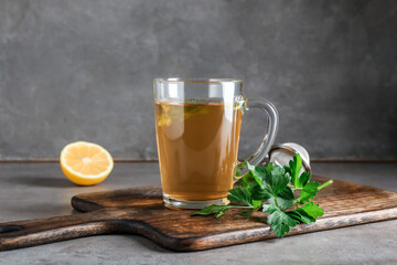 Board with cup of hot tea, parsley and lemon on grunge background