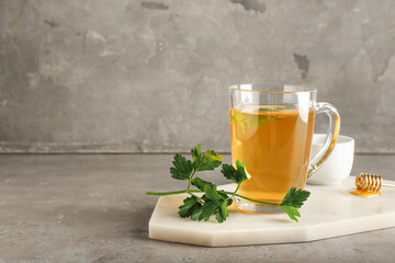 Board with cup of hot tea, parsley and honey on grunge background