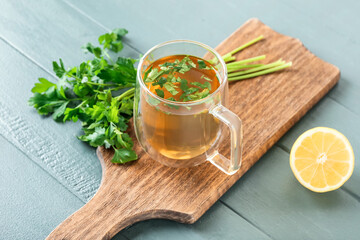 Board with cup of hot tea with parsley on color wooden background