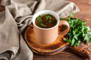 Board with cup of hot tea and parsley on wooden background