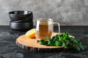 Board with cup of hot tea, parsley and lemon on dark background