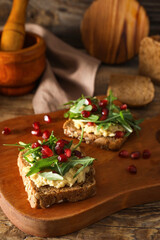 Tasty bruschettas with pomegranate and hummus on wooden background