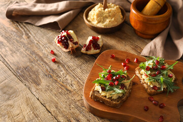 Tasty bruschettas with pomegranate and hummus on wooden background
