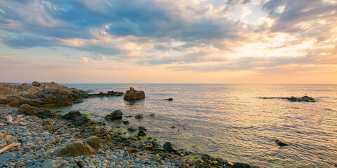 summer vacation scenery by the sea at sunrise. calm water washes pebble beach with stones and boulders. dramatic clouds above horizon in morning light on the sky