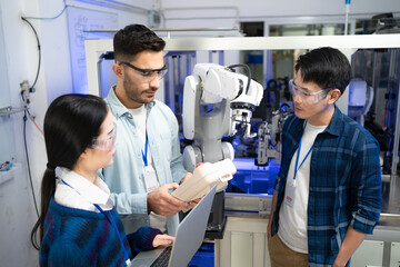 Caucasian male engineer standing hold a robot controller next to Asian female apprentice holding a laptop, listen intently to young Asian male CEO after demonstrated the work of robotic machine to him - obrazy, fototapety, plakaty