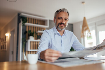 Portrait of a smiling middle aged businessman reading newspaper.
