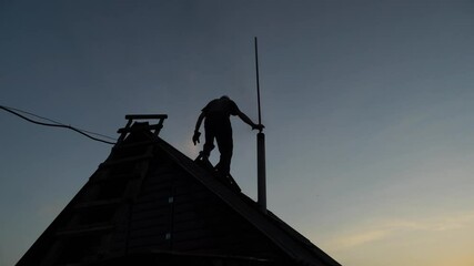 A male worker cleans a chimney on the roof at sunset in the late evening.Clean the soot in the chimney.Dioxides,harmful exhaust fumes,air and environmental pollution.Chimney and pipe cleaning service
