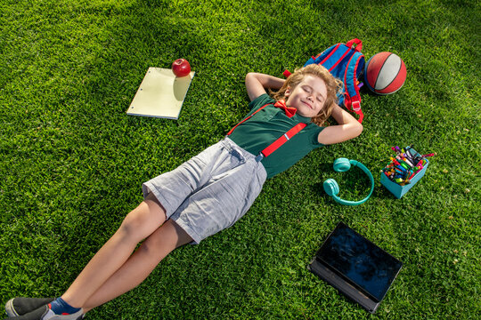 Kid with book and taplet and resting on the grass after school. Happy boy relaxing on the grass.