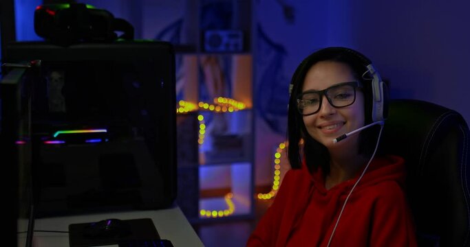 Portrait, a beautiful woman vlogger sits at the workplace at the computer in a dark room with backlight. Woman vlogger smiling and looking at the camera, happy woman, modern technologies of