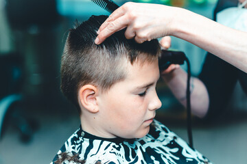Fototapeta premium Cute kid have hair cut,professional barber doing haircut. Hairdress for children. side view portrait barbershop.Toned