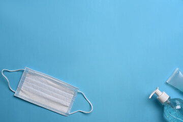 Protective mask and hand sanitizer gel on blue background.