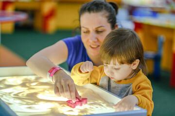 Creative early baby development. A mother teaches her child to draw with her fingers in the sand....