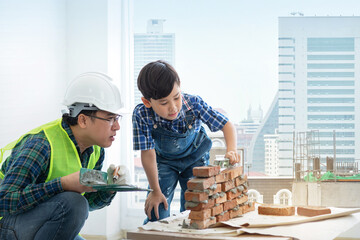 Child boy is learning to install installing brick masonry with an engineer father, building under...
