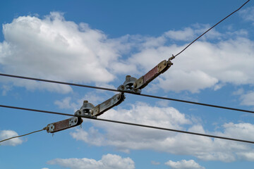 A fragment of the contact network of a public trolleybus on the background of a blue sky with white clouds