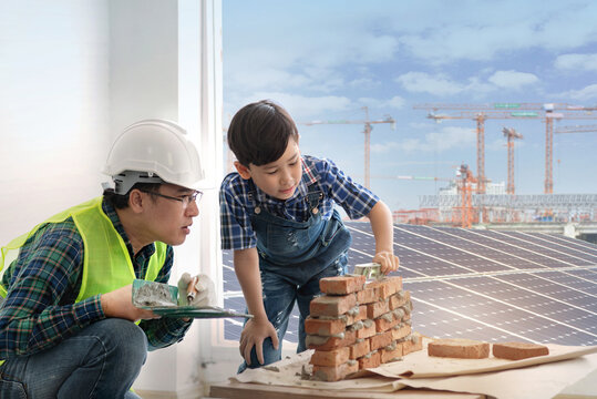 Child boy is learning to install installing brick masonry with an engineer father, Solar panel and crane in the background, Father and son concept - Powered by Adobe
