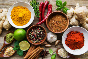 A selection of various colorful spices on a wooden table in bowls and spoons