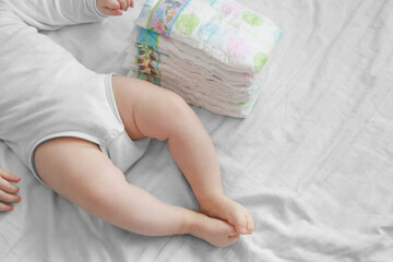 Baby feet and a pack of diapers on a white bed. Dirty diapers. Newborn and costs - obrazy, fototapety, plakaty