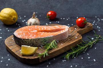 Raw salmon fillet with spices and vegetables on the graphite board.