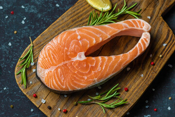 Raw trout fish steaks, pepper, salt and herbs on black wooden table