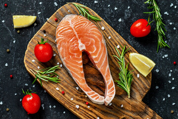 Fresh raw salmon steak with spices on dark wooden background.