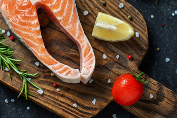 Fresh raw salmon fish steak with spices on dark wooden background.