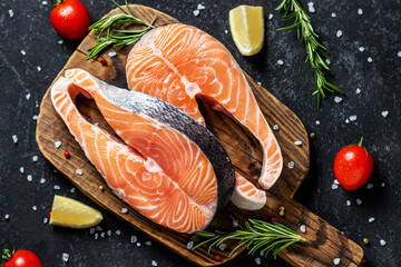 Two fresh raw salmon steaks with salt, peppers, lemon, tomatoes and rosemary on the rustic table