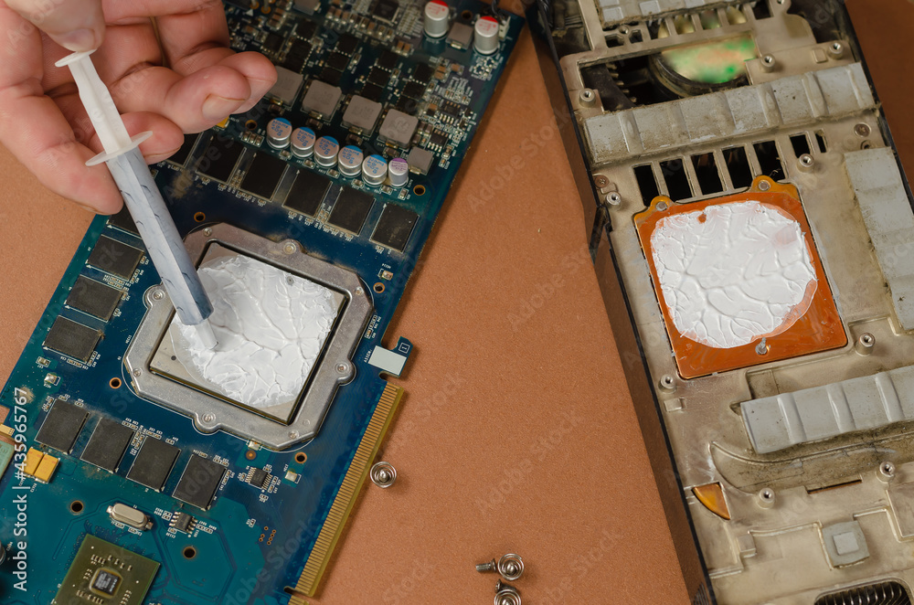 Fototapete computer graphics card on brown background. man puts new thermal paste on the processor with a syrin