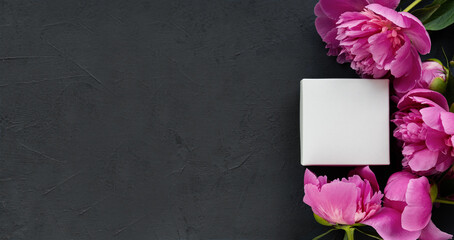 Small white box in a frame of pink delicate peonies on a beautiful black cement background . Romantic concept. Flat lay.Postcard.Place for text