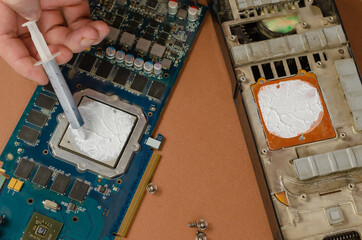 Computer graphics card on brown background. Man puts new thermal paste on the processor with a...