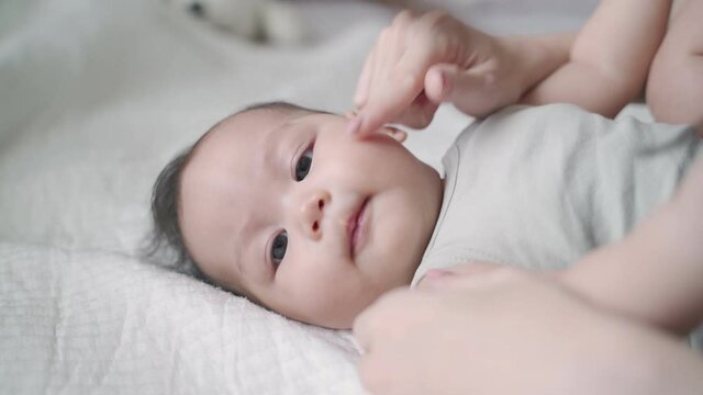 asian woman mother play and kissing baby infant on cheek softly on bed. baby happy when mother parent kissing with love and care. mom using nose touching kiss daughter at home. authentic lifestyle.