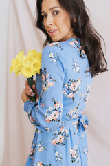 Spring indoor portrait of smiling woman with yellow flowers bouquet wearing femine dress. Young happy girl with spring yellow iris on beige background lifestyle photo.