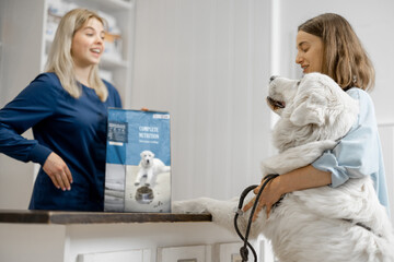 Female owner with big white dog on reception in veterinary clinic choosing dry food for the pet....