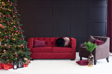 Thevelor sofa in the dark loft room has a bright light from the eternal light and an artificial fireplace. Inner attic with concrete walls and a decorated Christmas tree with gift boxes